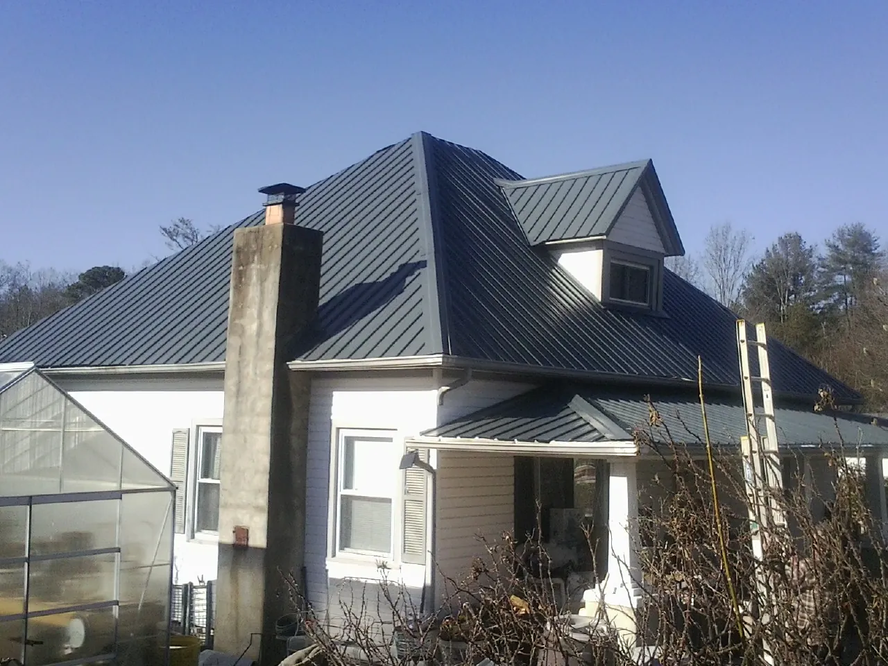Dark blue standing seam metal roof on a white farmhouse with dormer — Slate & Tile Roof Repair by Roofing Brothers in Oldsmar