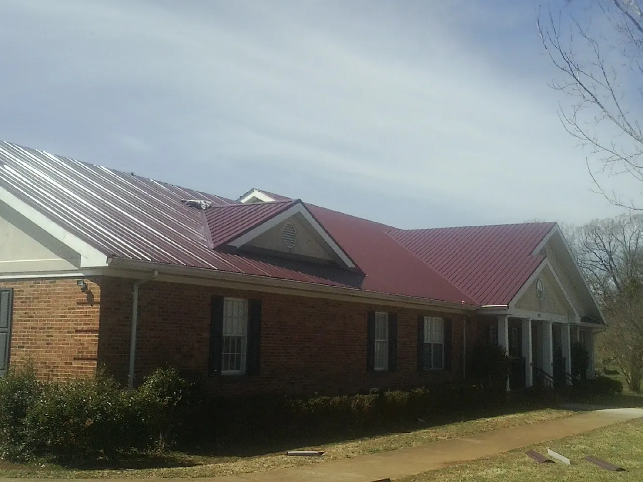 Red metal roof with gabled entries on a long brick building, from a Hail Damage Roof Repair job in Oldsmar