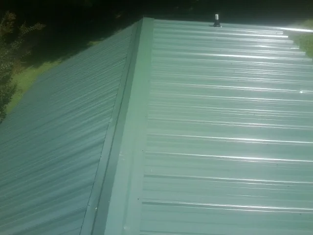 New green metal panels meeting at the ridge of a roof — Flat Roof Repair work by our crew in Oldsmar