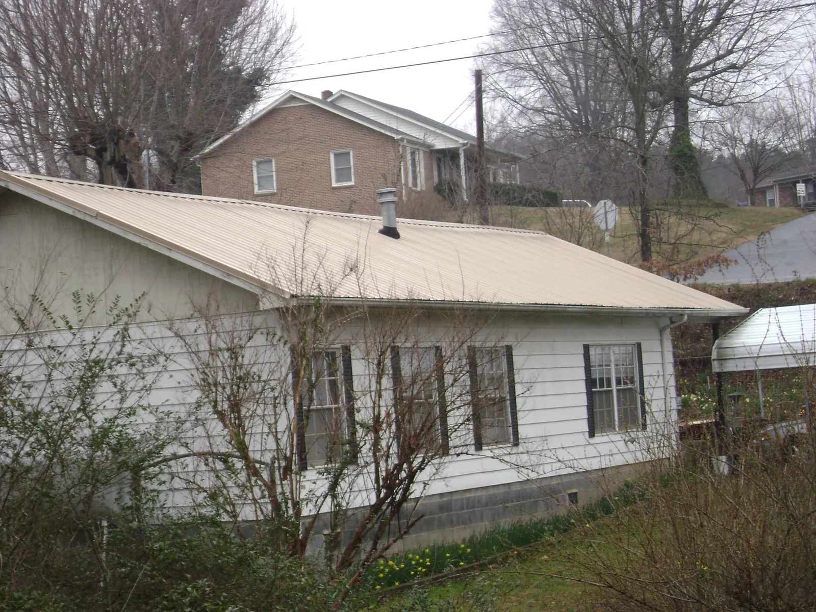 Tan metal roof on a white sided house set into a hillside — Commercial Roofing by Roofing Brothers in Oldsmar