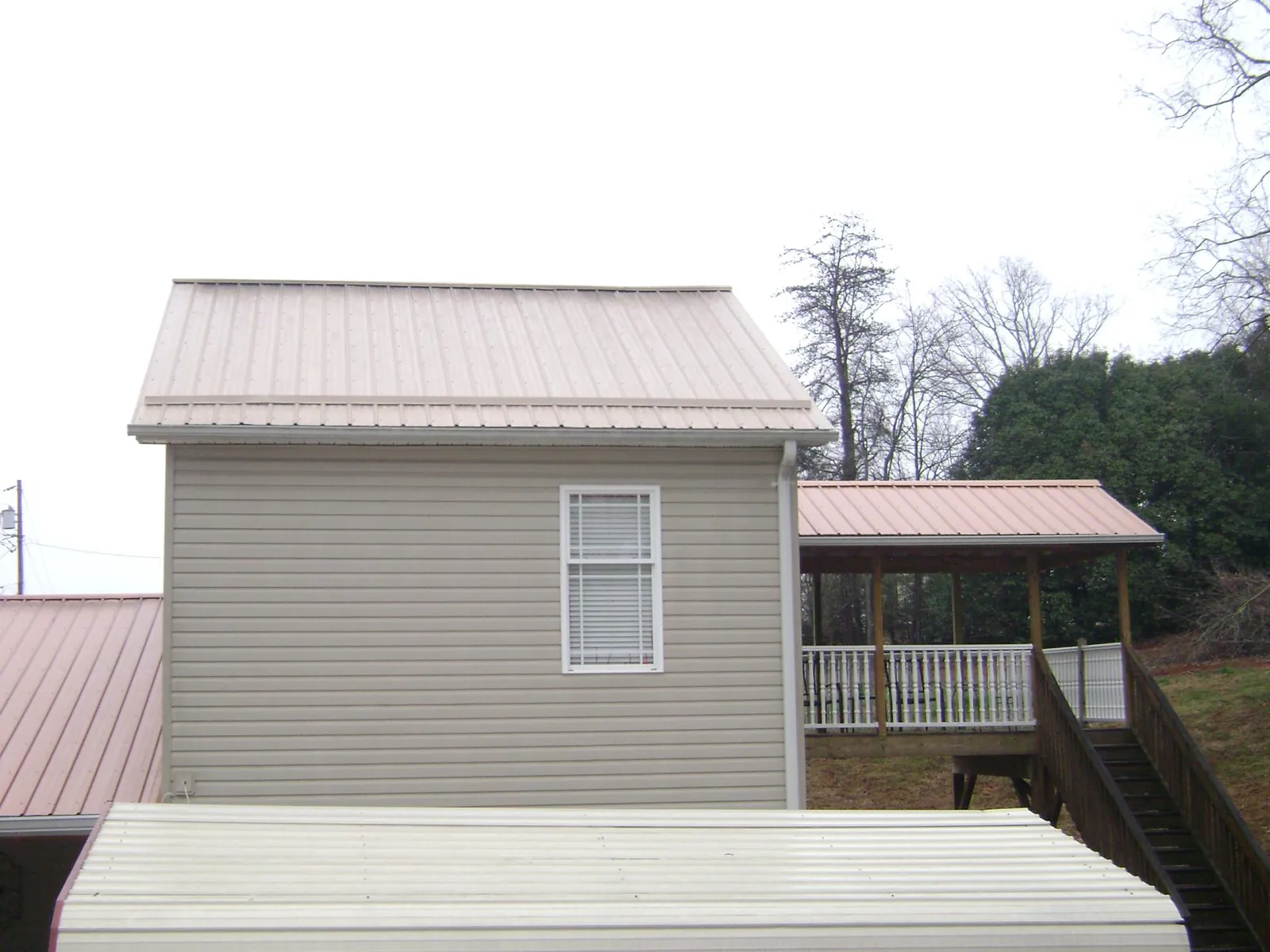 Tan metal roofs on a two story addition and attached porch, from a Roof Replacement job in Oldsmar